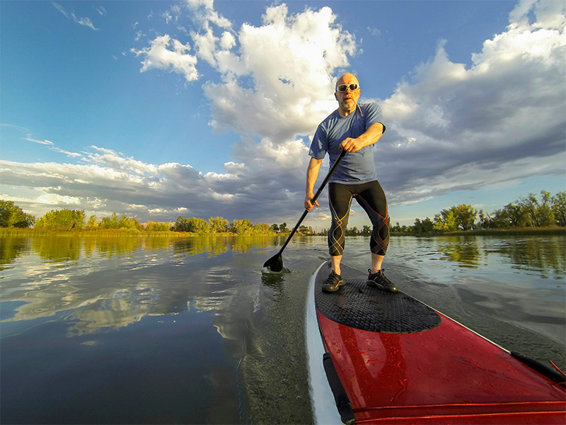 Older man standing on paddle board in water